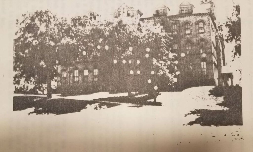 A vintage-style, high-contrast image of a large brick building with trees in the foreground.