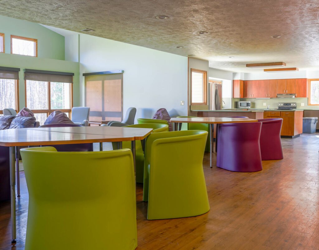 A communal space with colorful chairs and tables, possibly in a group home or shared accommodation setting.