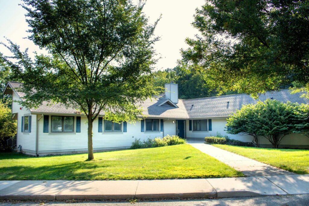 A single-story house with a manicured lawn, trees, and a concrete path leading to the entrance.