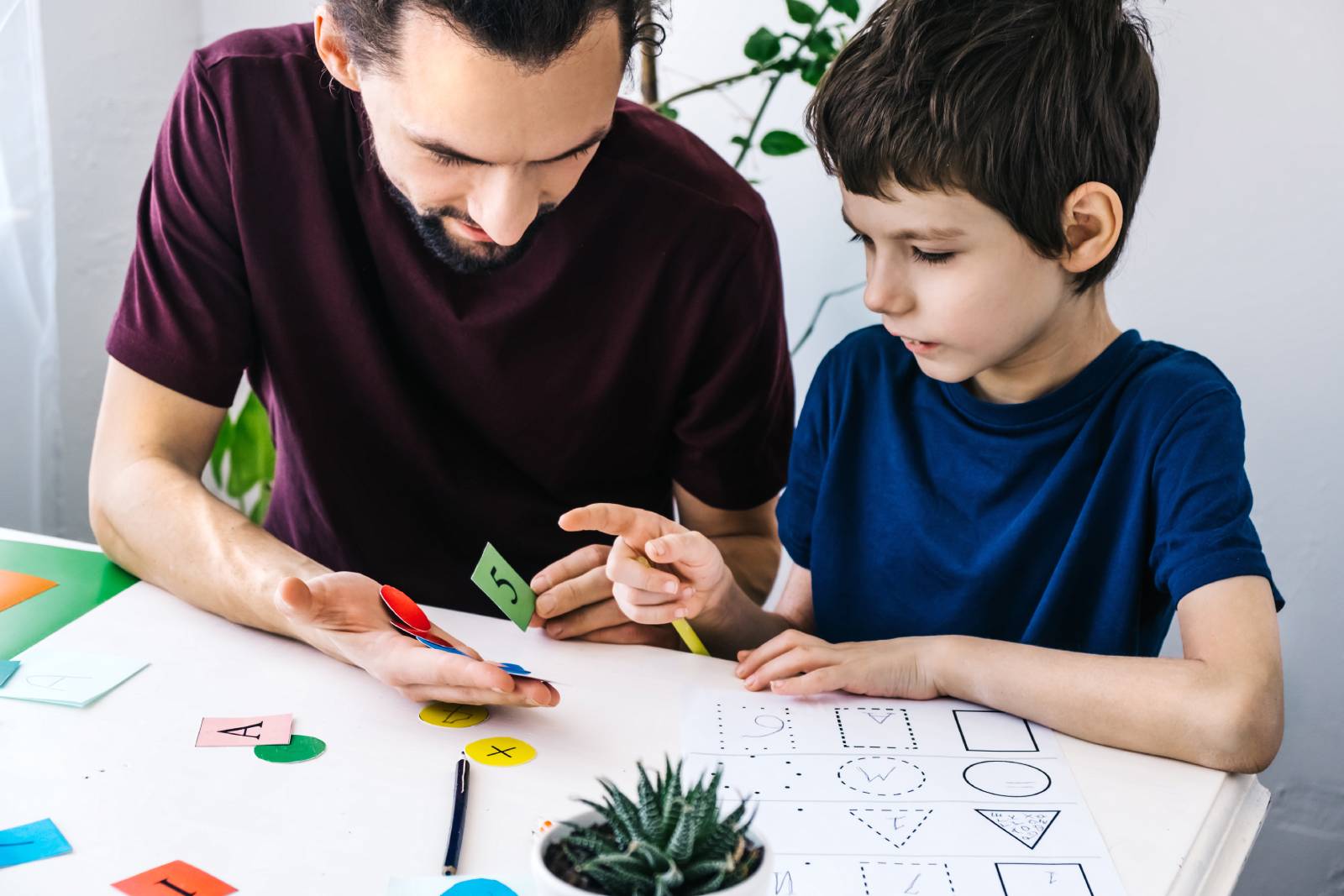A man and a child are engaged in a learning activity with colored cards and worksheets.