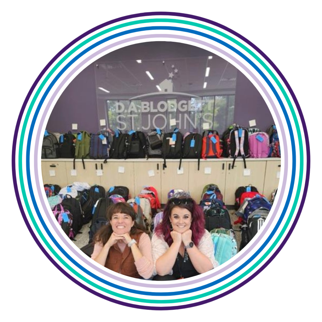 Two people smiling in front of a display of backpacks. Could be part of a 2026 back to school drive.