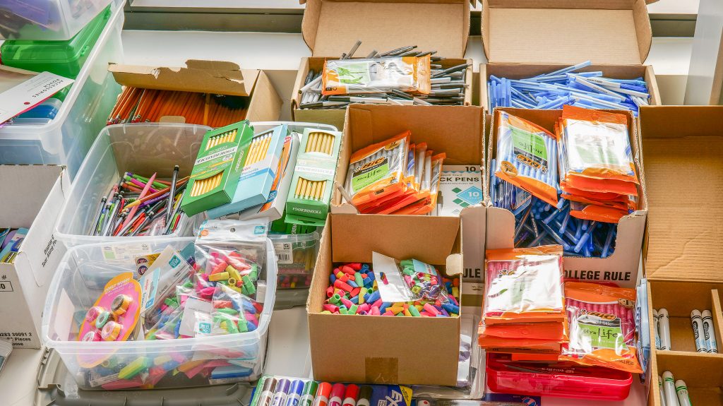 Assorted school supplies including pencils, pens, erasers, and markers in boxes, suitable for a 2026 back to school drive.