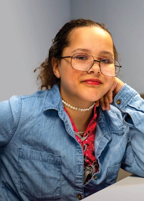 A person wearing glasses, a denim shirt, and a pink top.