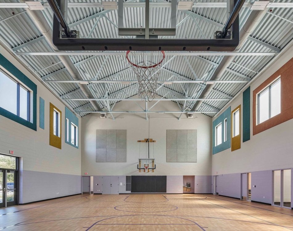 An empty indoor basketball court with bright walls and ceiling beams.
