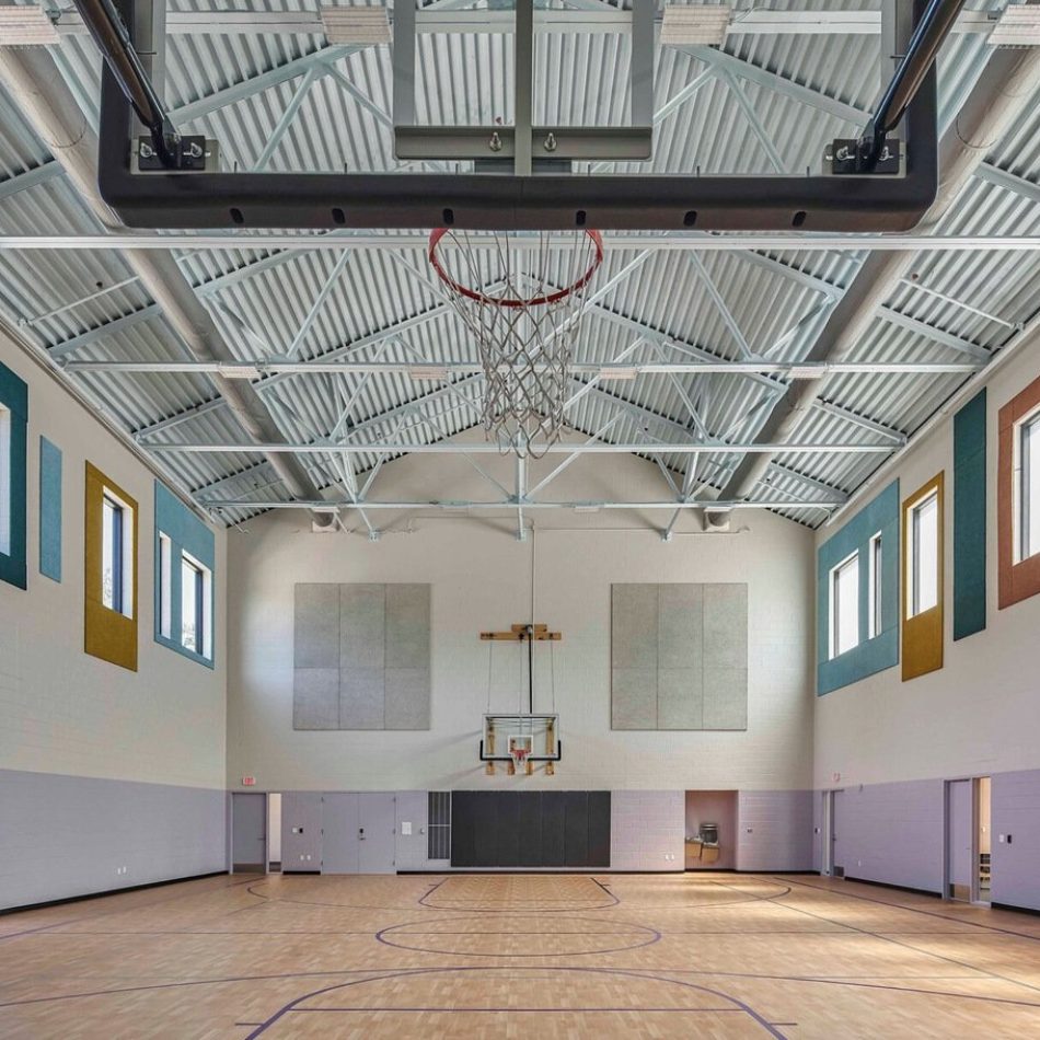 An empty indoor basketball court with bright walls and ceiling beams.